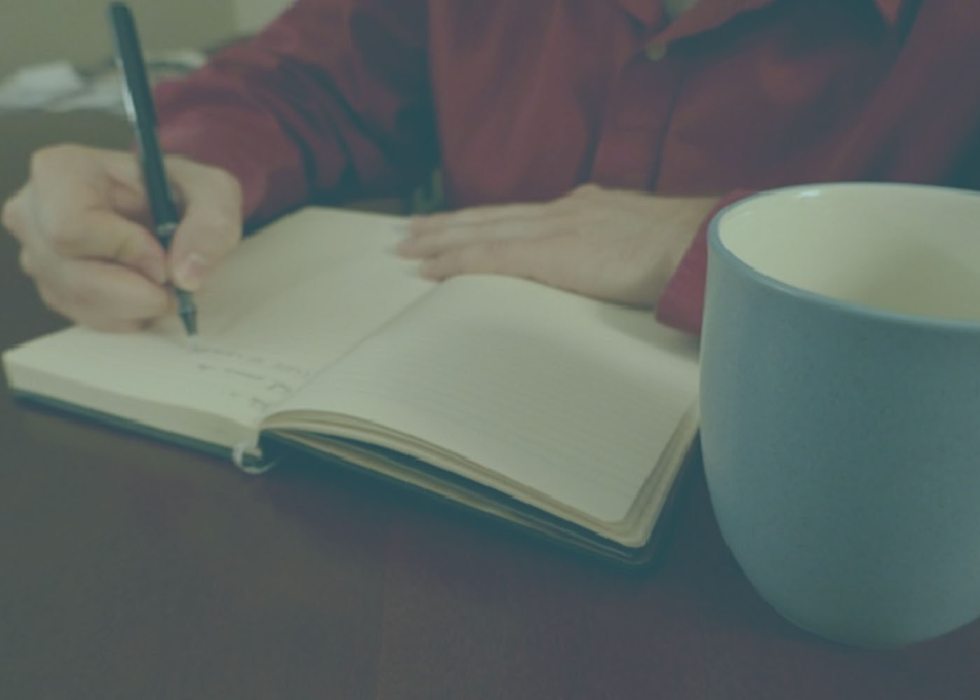 Person writing in journal with cup of tea next to them